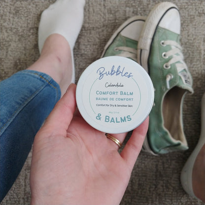 Calendula Comfort Balm from Bubbles &amp; Balms in the hands of a woman getting ready to use it for foot care.